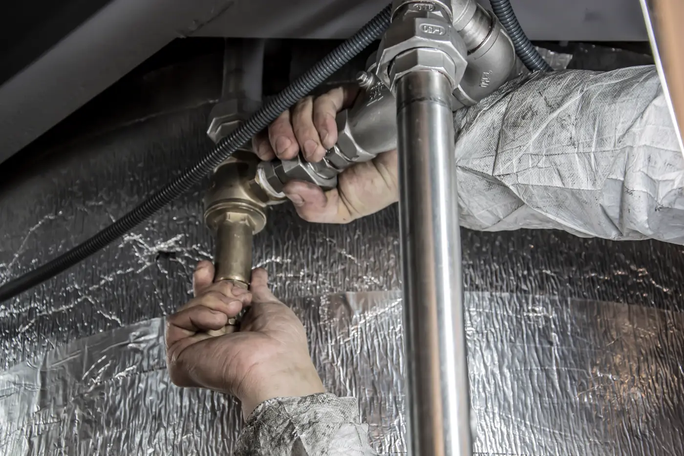 A plumber tightening a brass fitting on a water line